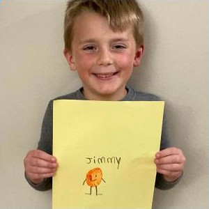 A boy holding a yellow page with his drawing of a Thumby