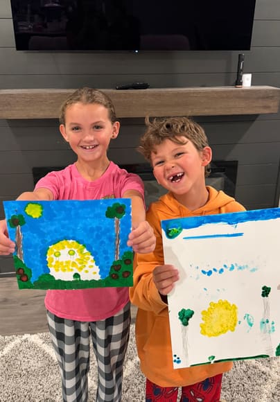Two kids holding up their paintings
