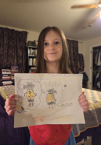 A girl holding up her drawing of two Thumbies