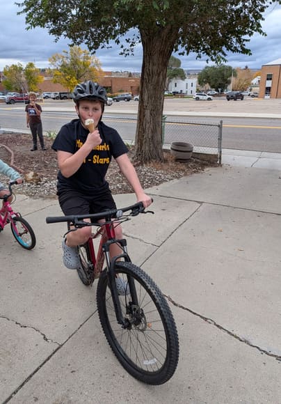 A boy riding a bike while eating an ice cream cone