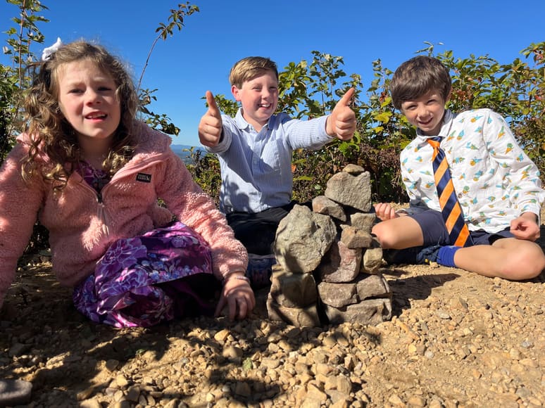 Three kids outside beside a stack of rocks