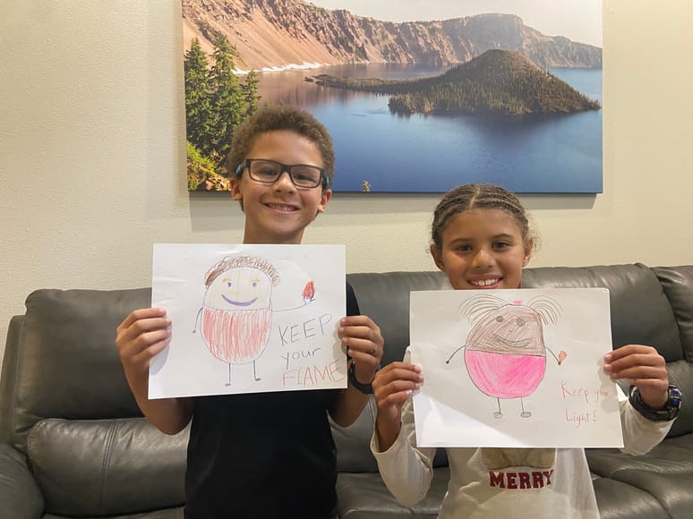 Two kids on a couch holding up their drawings